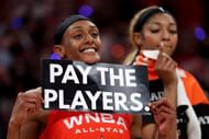 Brittney Sykes #15 of the Washington Mystics holds a "Pay the Players" sign next to Angel Reese #5 of the Chicago Sky following the 2025 AT&T WNBA All-Star Game at Gainbridge Fieldhouse on July 19, 2025 in Indianapolis, Indiana. - Source: Getty